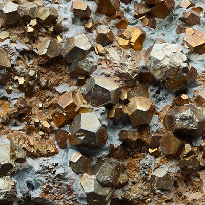 Pyrite pyritohedron crystals densely covering clay-like matrix surface