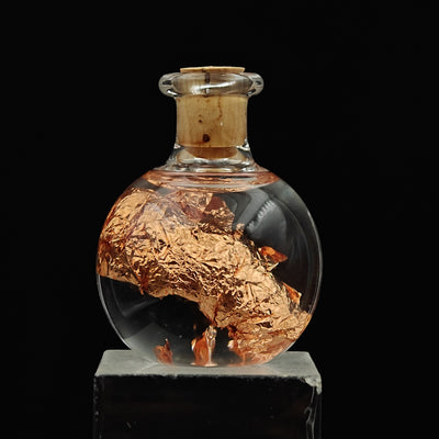 Native copper foil leaf curled inside clear glass vial on stand
