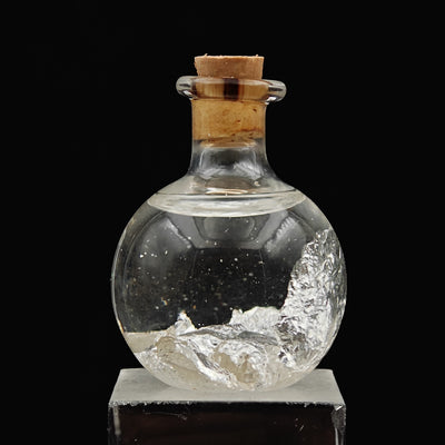 Silver leaf flakes settled at base of glass vial with cork stopper
