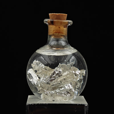 Round glass bottle with cork stopper filled with silver leaf flakes