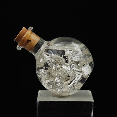 Side view of corked glass vial containing natural silver leaf flakes